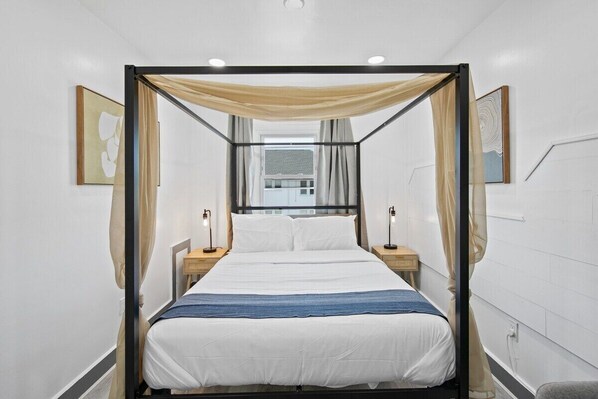 A modern bedroom with a canopy bed, bedside lamps, and artwork on the walls.