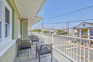 A balcony with two chairs and a table, a white railing, and a view of a street with buildings.