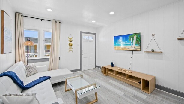 A modern living room with a white sofa, glass coffee table, wooden bench, and a painting of a beach scene.