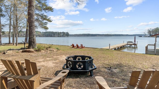 Une terrasse au bord du lac, avec des chaises en bois, un foyer et une jetée qui s’avance dans l’eau.