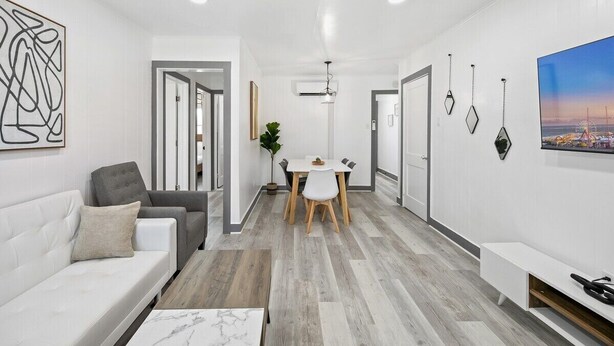 A modern living room with a white sofa, a grey armchair, a dining table with chairs, and a white bench. - Shorehaven 7- Updated and Stylish 2 bedroom 14 St! (Ocean City)