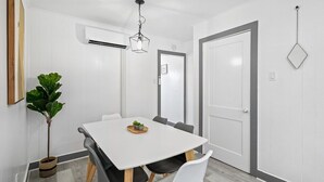 A dining area with a white table, black and white chairs, a hanging light fixture, and a potted plant. - Shorehaven 7- Updated and Stylish 2 bedroom 14 St! (Ocean City)
