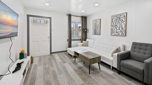 A modern living room with a white sofa, a grey armchair, a wooden coffee table, and abstract wall art. - Shorehaven 7- Updated and Stylish 2 bedroom 14 St! (Ocean City)