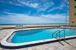 A swimming pool with a view of the ocean, a lifeguard stand, and lounge chairs.