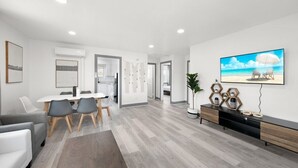 A modern living room with a dining area, a kitchen, and a large TV on the wall.