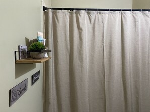 A bathroom with a beige shower curtain, a wooden shelf with a potted plant, and two nameplates on the wall.
