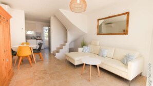 Una sala moderna con un sofá, una mesa de centro y un comedor con sillas y una mesa. Se ve una escalera que sube a otro nivel.