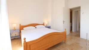 Un dormitorio con una cama de madera, dos mesitas de noche con lámparas y una puerta que da a otra habitación.