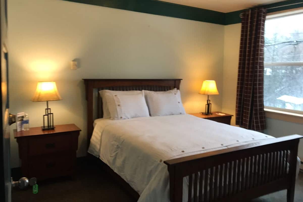 Un dormitorio con cama, dos mesitas de noche con lámparas, una ventana con cortinas y una puerta con llave.