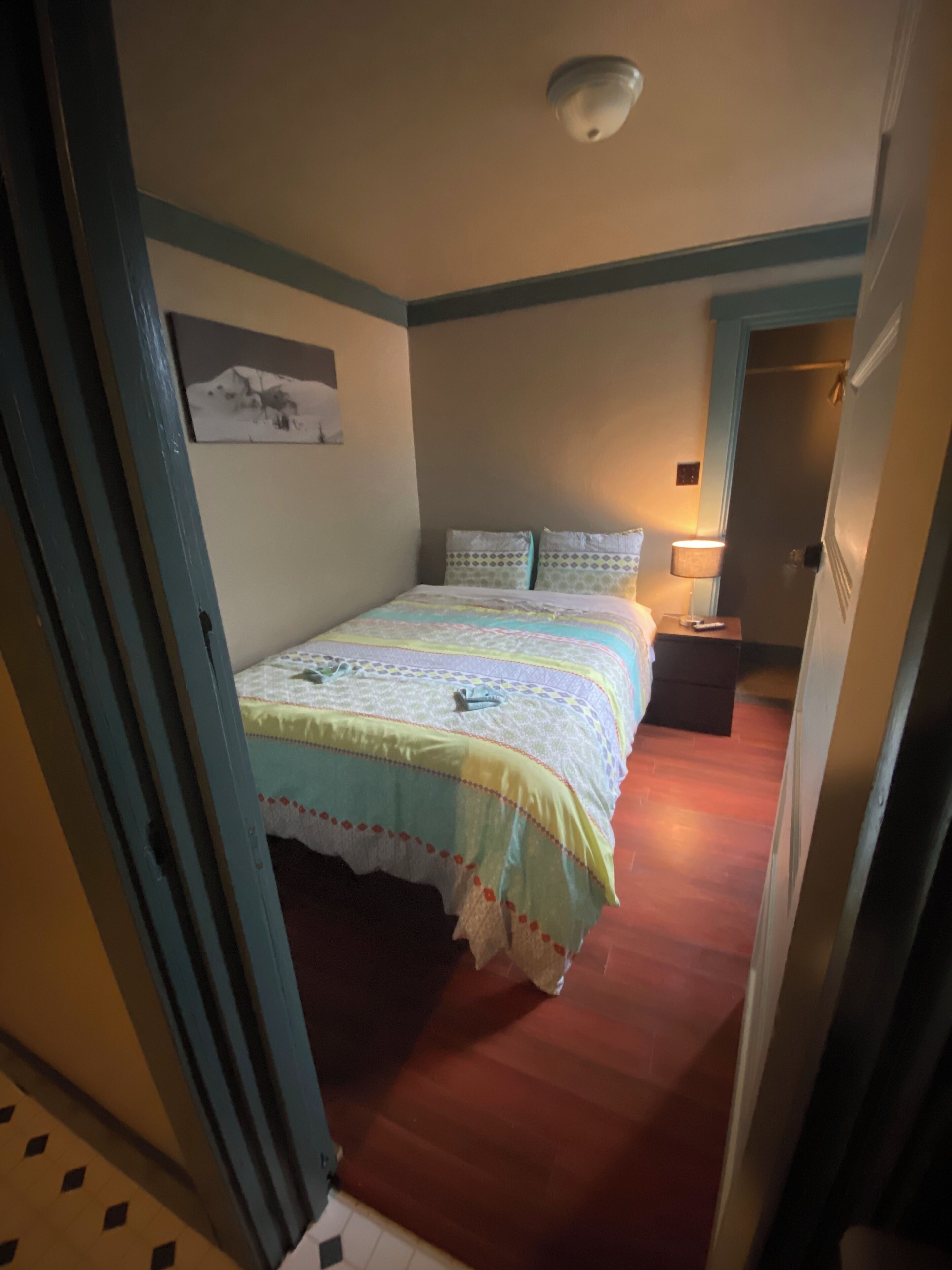 A bedroom with a bed, a nightstand, a lamp, and a door.
