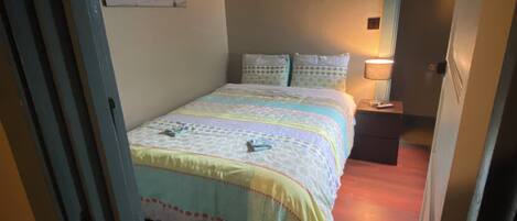 A bedroom with a bed, a nightstand, a lamp, and a door.