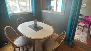 A dining area with a round table, four chairs, a window with curtains, a mirror, and a wooden ceiling. - Historic Hotel Bayview (Stewart)