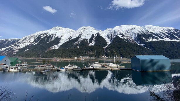 A marina with boats docked, a clear sky, and snow-capped mountains in the background. - Historic Hotel Bayview (Stewart)
