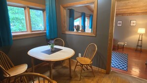 A room with a round wooden table, four wooden chairs, a mirror on the wall, and a window with curtains. - Historic Hotel Bayview (Stewart)