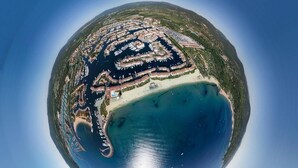 Luchtbeeld van een kustgebied met een jachthaven, zandstrand en woongebouwen.