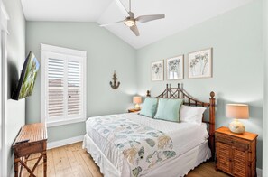 A bedroom with a bed, a ceiling fan, a TV, a window with blinds, and a bedside table. - Great Location | Shared Heated Pool | Pet-Friendly (Port Aransas)