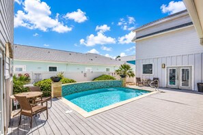 A pool with a wooden deck, outdoor furniture, and a building with a light blue exterior. - Great Location | Shared Heated Pool | Pet-Friendly (Port Aransas)