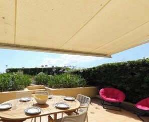 An outdoor patio with a round table set for dining, surrounded by chairs, under a canopy. - 3 bedrooms appartment on the beach, with air conditioning + WIFI (PORT GRIMAUD)