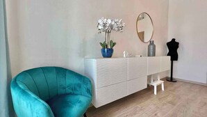A teal armchair, a white vanity with a mirror, a potted orchid, and a mannequin bust.