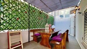 An outdoor patio with a wooden table and benches, a decorative wall with green foliage, and a hanging lantern.