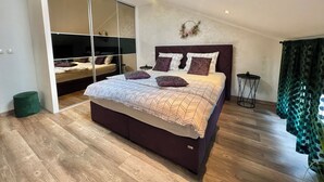 A modern bedroom with a large bed, a sliding glass door closet, and a small side table.