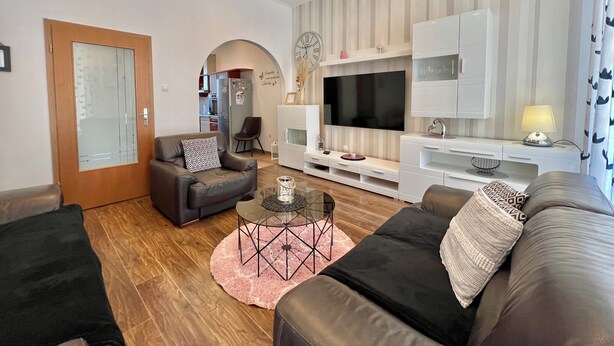 A modern living room with a sofa, a coffee table, a TV, and a kitchen in the background.