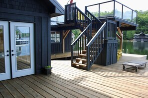 A wooden deck with a glass door, a staircase, and a small table. - Modern Muskoka Gem with Gorgeous Lake View, Sleeps 10 -Minimum Stay 28 days (Minett)