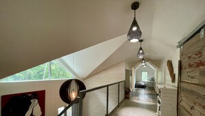 Een ruime gang met een hoge plafond, een trap met metalen leuning, en een zicht op een keuken in de verte.