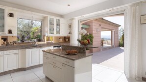A spacious kitchen with white cabinetry, granite countertops, and a view to an outdoor patio. - Charming 6-bedroom villa (Mouans-Sartoux)