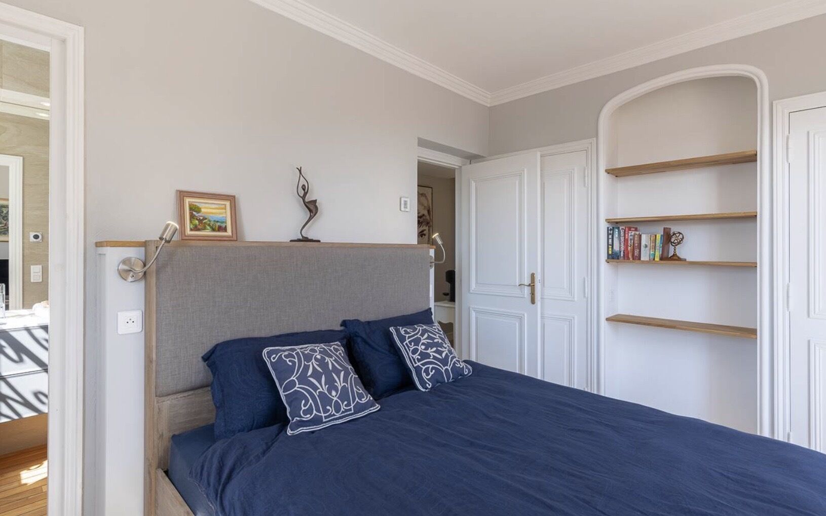 Ein Schlafzimmer mit Bett, Nachttisch, Lampe, Tür und Bücherregal.