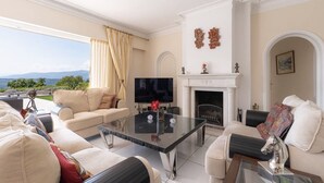A spacious living room with a sofa set, a glass coffee table, a fireplace, and a TV. - Charming 6-bedroom villa (Mouans-Sartoux)