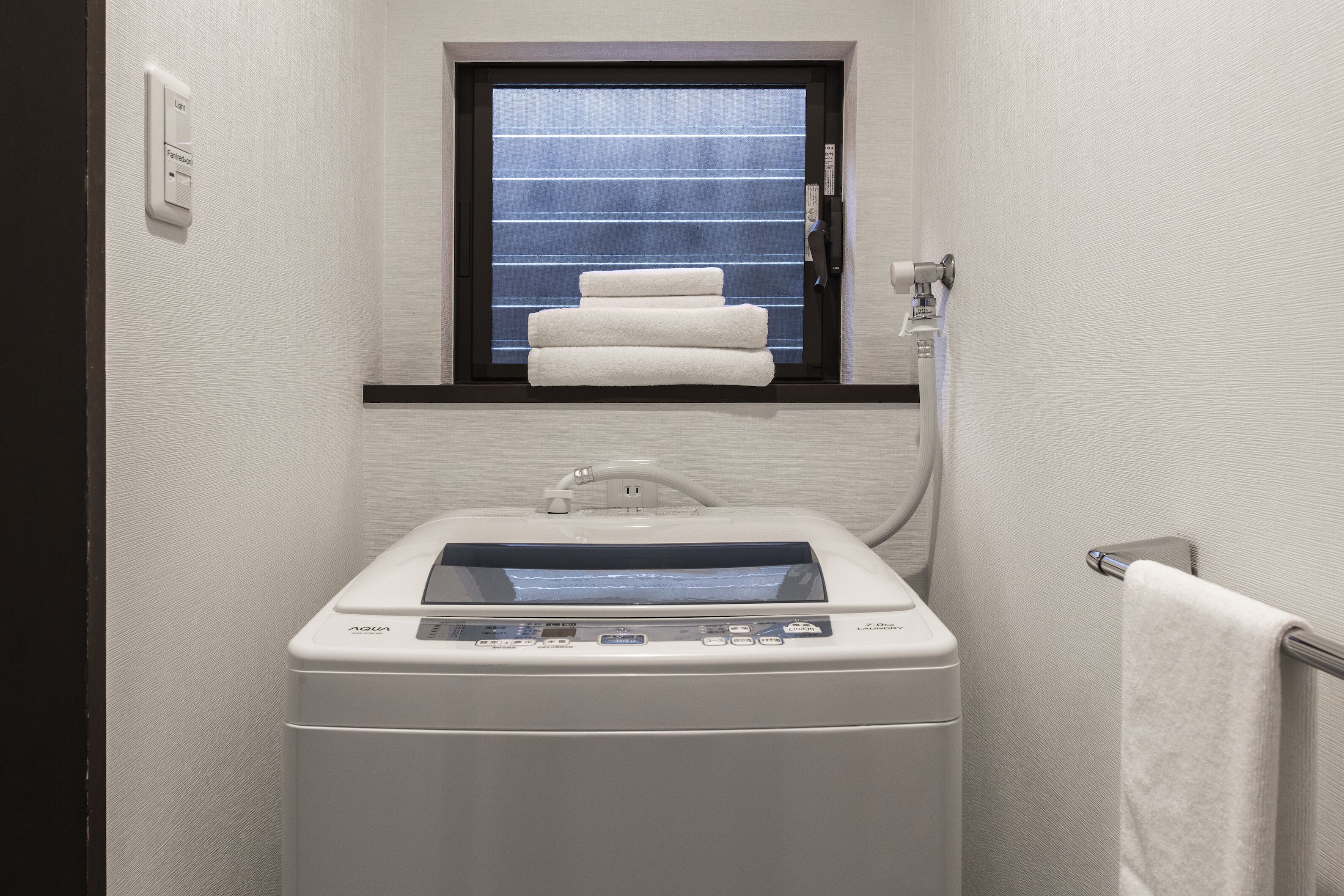 Een compacte, moderne badkamer met een ingebouwde wasmachine en droger, een raam met handdoekhouder, en een handdoek aan de muur.