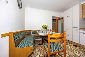 A dining area with a wooden bench, a table set with plates and a vase of flowers, and a stone-tiled floor.