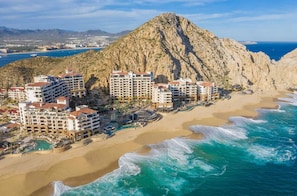 A coastal resort with multiple hotel buildings, a sandy beach, and a rocky mountain in the background.
