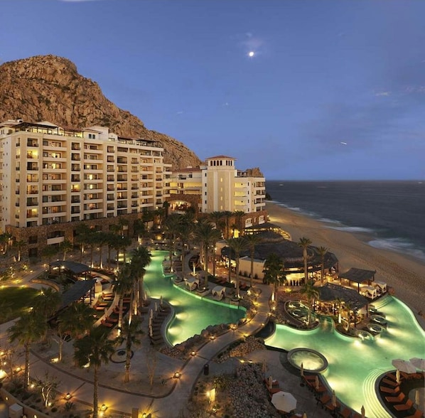 A resort with multiple buildings, a pool area, and a beach view.