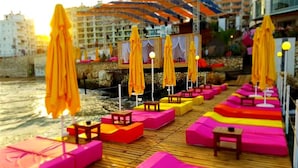 En terrasse med farverige siddepladser og parasoller med udsigt over en strand.