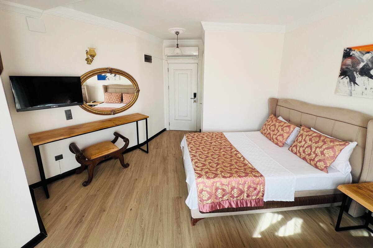 A bedroom with a bed, a desk, a chair, a television, and a mirror.