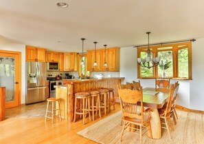 A spacious kitchen with wooden cabinets, a stainless steel refrigerator, and a bar area with stools. - Hunter Mountain Luxury Cabin | Hot Tub | Fire Pit (Hunter)