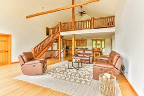 A spacious living area with a high ceiling, a wooden staircase, leather sofas, and a dining area. - Hunter Mountain Luxury Cabin | Hot Tub | Fire Pit (Hunter)