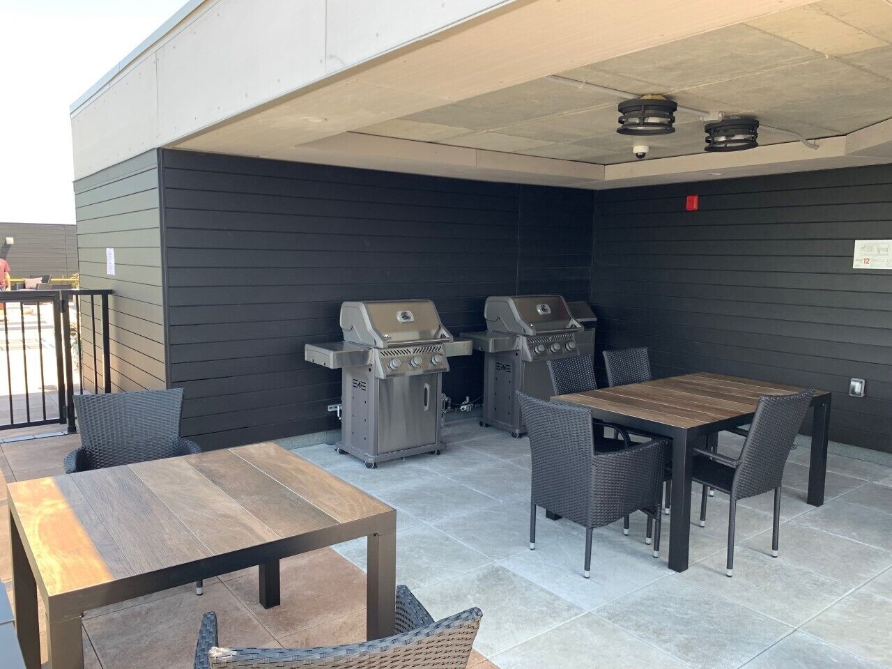 Un patio al aire libre con dos parrillas de barbacoa, una mesa de madera y sillas de mimbre.