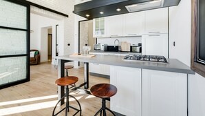 Une cuisine moderne avec des meubles blancs, un îlot central doté de tabourets et une cuisinière visible.