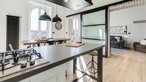 Une cuisine moderne dotée d’un îlot central, de luminaires suspendus noirs et d’une grande fenêtre.