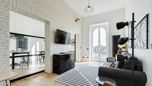 Un salon moderne avec un mur en briques blanches, un téléviseur à écran plat, un canapé noir, un tapis à rayures et une grande fenêtre.
