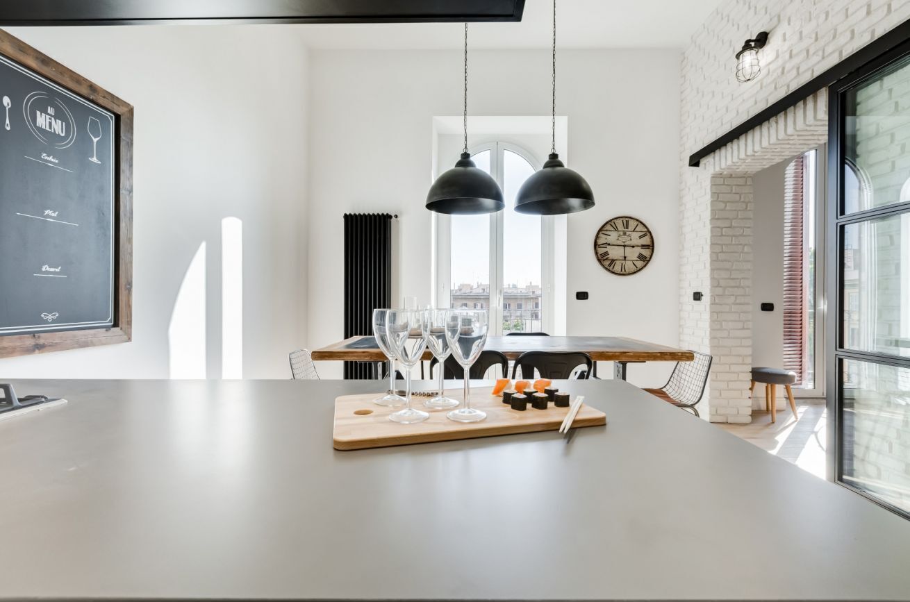 Une cuisine moderne dotée d’un îlot central, de luminaires suspendus, d’un tableau noir servant de menu et offrant une vue sur la ville grâce à de grandes fenêtres.