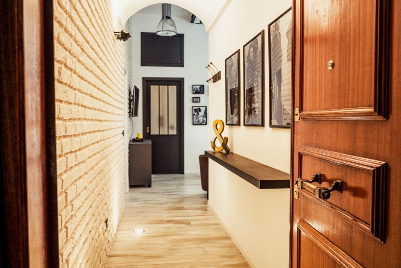A hallway with a brick wall, wooden floor, a wooden door, and a dark-colored counter with a small sculpture.