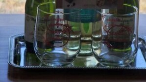 A tray with two bottles of Russell Stover wine and two glasses on a table with a view of a baseball field in the background.