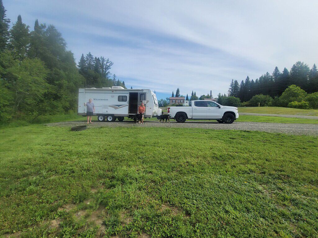 A white pickup truck towing a recreational vehicle in a grassy area with trees in the background.
