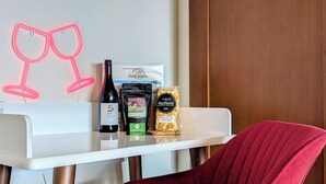 Une chambre d’hôtel avec une table blanche sur laquelle sont posés une bouteille de vin, une bouteille de champagne et un sachet de pop-corn gastronomique.