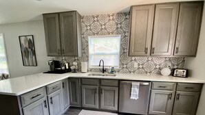 A kitchen with gray cabinets, a white countertop, and a patterned backsplash.