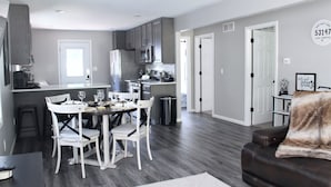 A modern kitchen with grey cabinets, a dining area with white chairs, and a leather sofa.